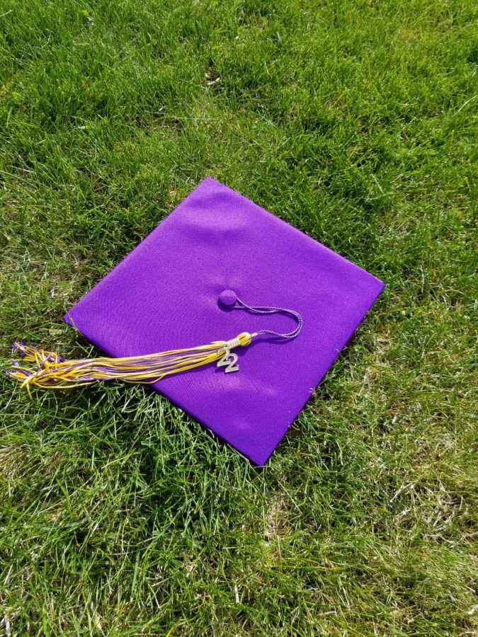 This picture shows a purple grad hat with a purple and yellow tassle with a gold 22 hanging off the side. It sits in green grass.