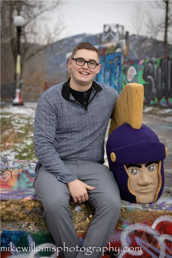 This+image+shows+a+guy+sitting+on+a+graffiti+covered+ledge+with+the+helmet+of+the+mascot+costume+for+a+spartan.+He+is+wearing+grey+slacks+and+a+long+sleeve+fitted+sweater.+He+is+smiling+at+the+camera.