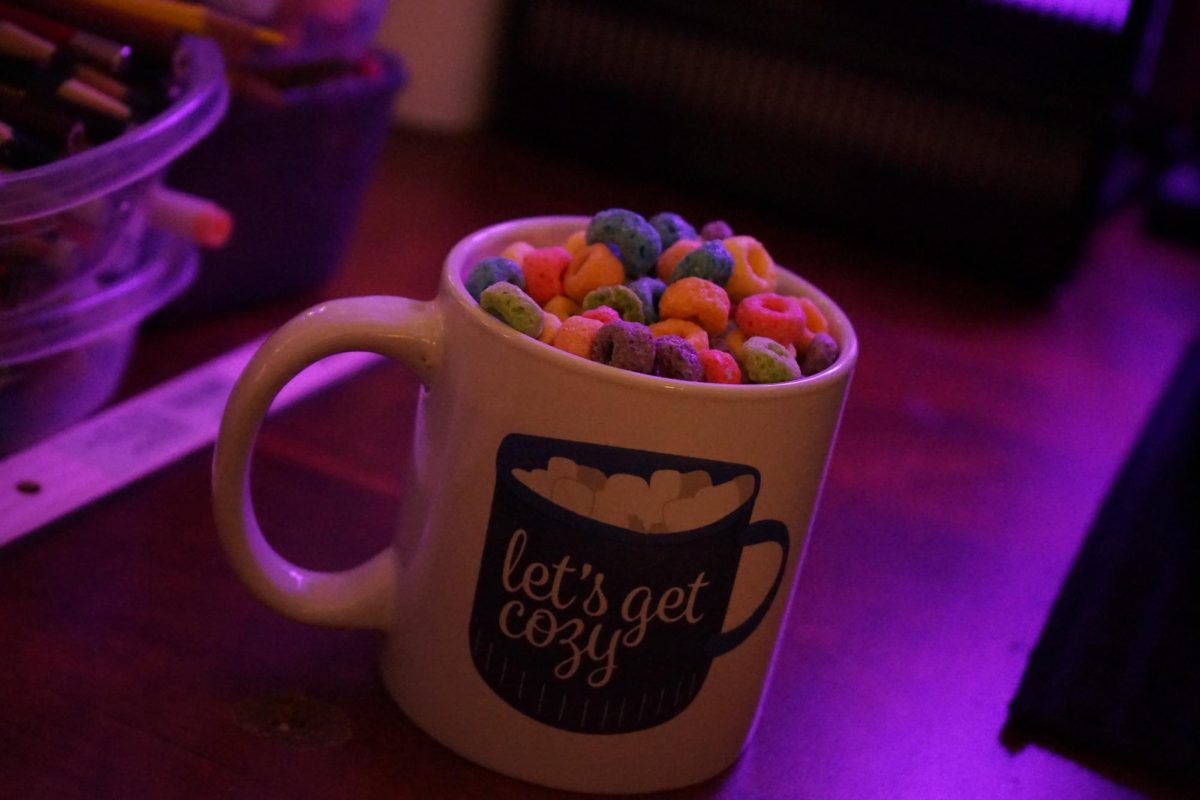 A picture of fruit loops in a mug that says Lets Get Cozy in dim purple lighting.