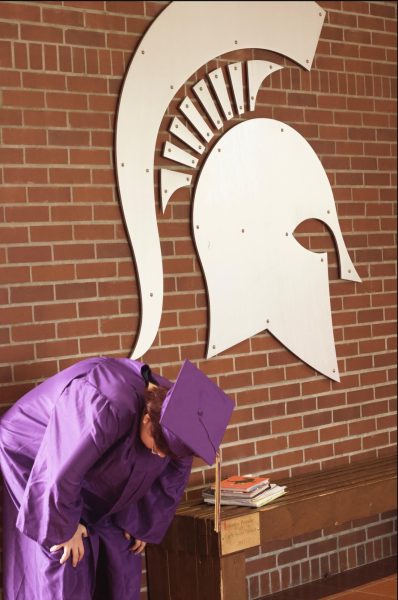 Teen in cap and gown catching their breath by the Spartan symbol